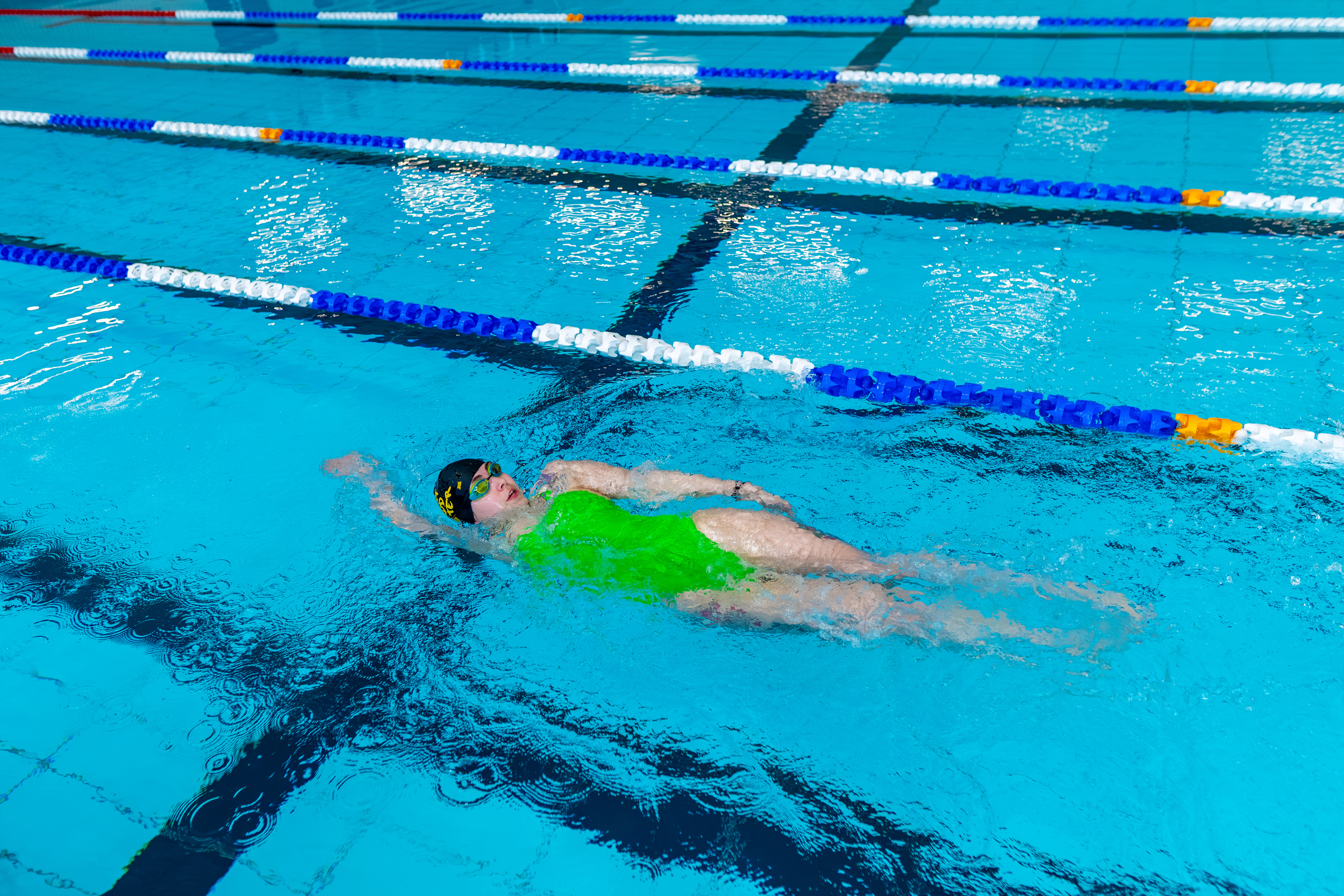 Lady swimming at Highlight wearing a navy swim cap, goggles and lime green swimming costume