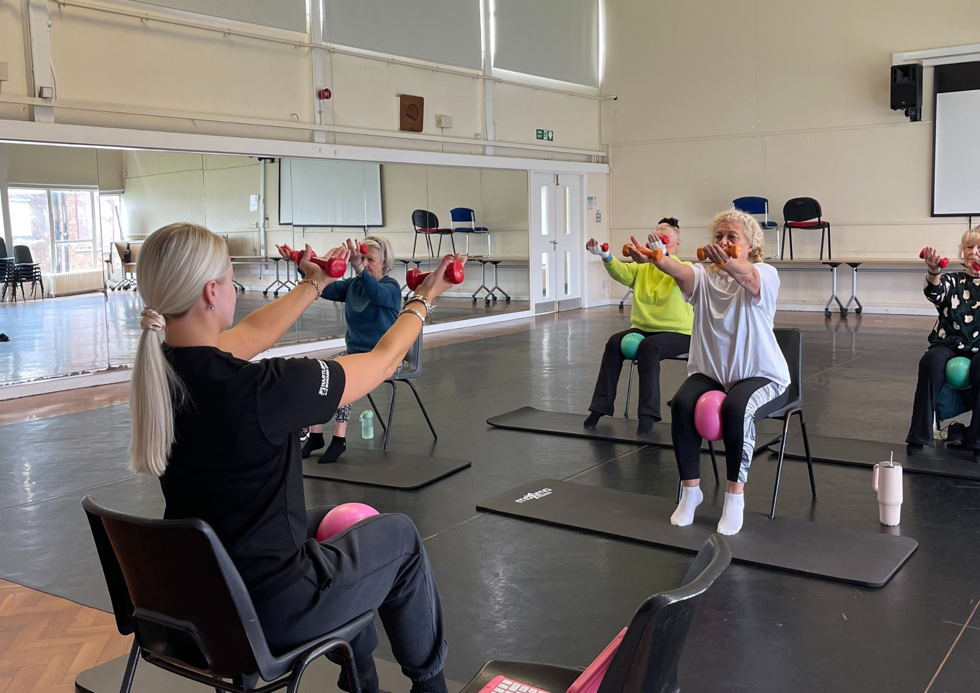 The image shows an instructor teaching chair pilates to 4 women.