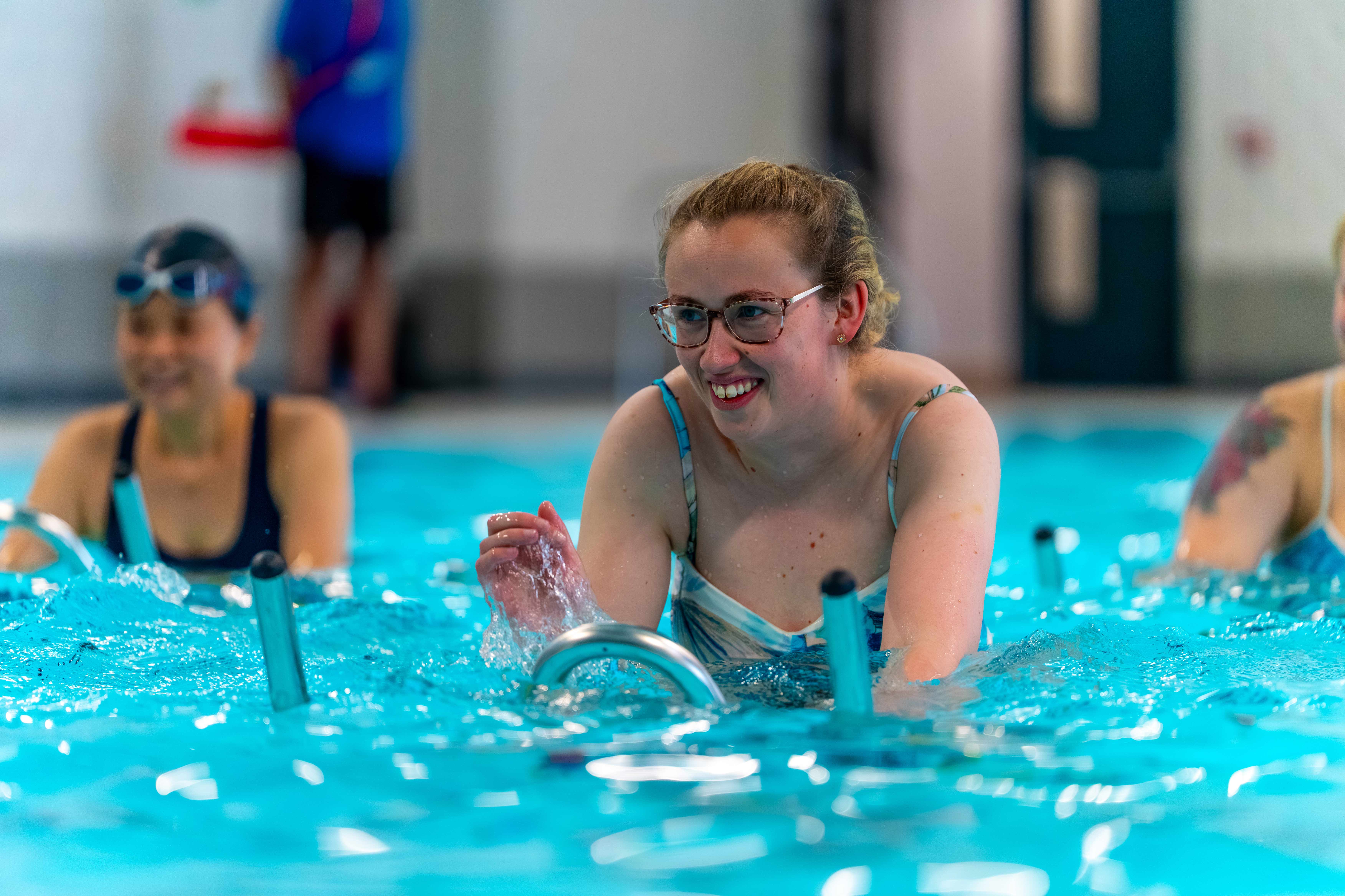 A blonde haired lady with glasses cycling in water on a aqua spin bike