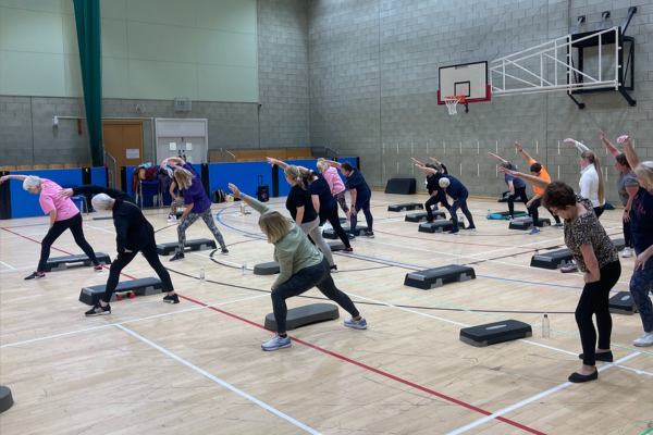 Step and tone fitness class with people stretching to one side with arms up in the air