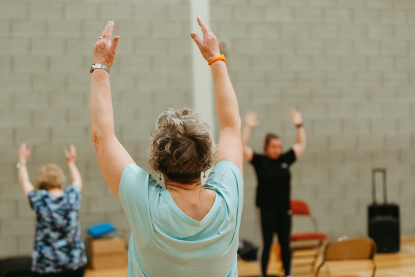 Woman wearing a light green tshirt, lifting her arms up to stretch