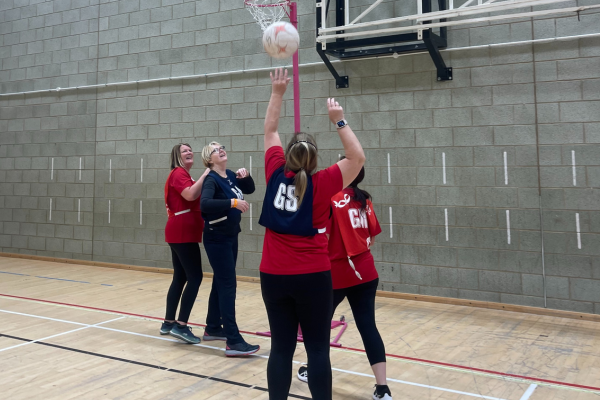 A group of ladies playing walking netball in red t-shirts and navy bibs.