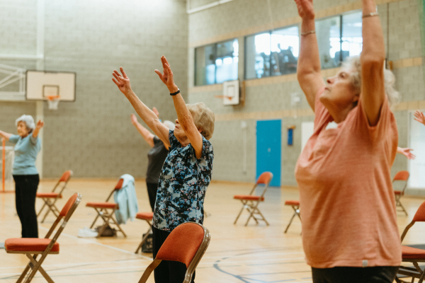 The photograph shows women stretching with their arms up in the air